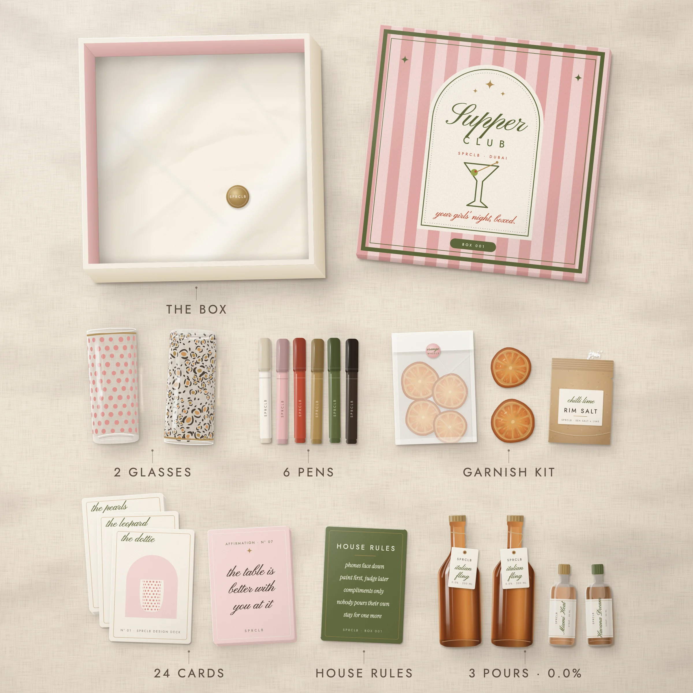 Everything in Box 001 laid out from above: the box and its striped lid, two painted highball glasses, six pens, the card decks, the garnish kit, the house rules and the three pours